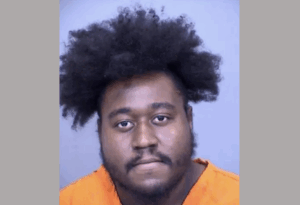 Portrait of a man with a serious expression, wearing an orange jumpsuit.