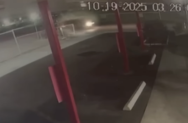 Blurry headlights are visible on a street at night, captured by security cameras in a dimly lit parking area with several red posts.