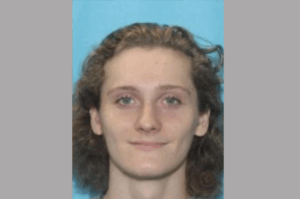 Portrait of a person with curly brown hair, blue eyes, and a slight smile, photographed on a blue backdrop.