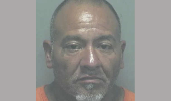 Close-up image of a man in a booking photo, with a serious face and gray goatee, dressed in orange jail clothing.