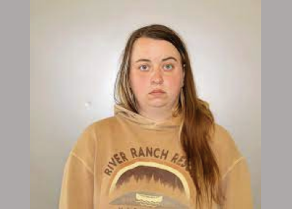 Individual in a tan "River Ranch Resort" sweatshirt poses for a photo in front of a plain wall, looking directly forward.