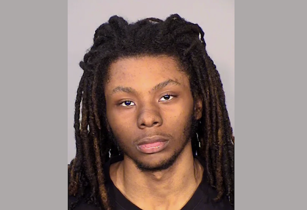 Portrait of a male individual with shoulder-length dreadlocks, wearing a black shirt, photographed head-on in a standard booking photo setting.