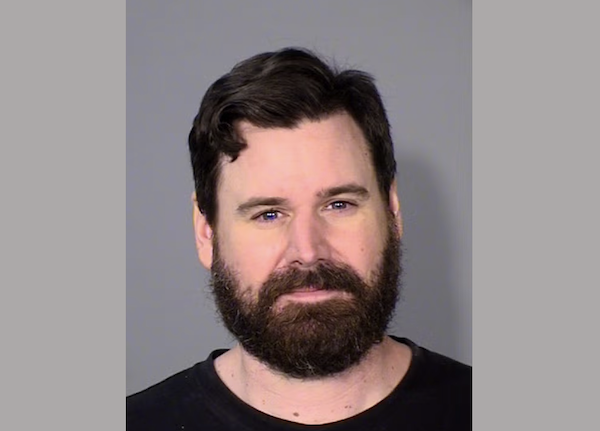 Portrait of a bearded man with short, dark hair in front of a neutral backdrop, gazing directly at the camera.
