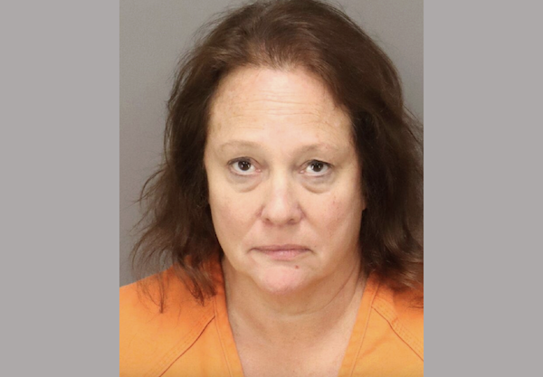 Middle-aged woman wearing an orange prison jumpsuit, photographed from the shoulders up in a booking photo.