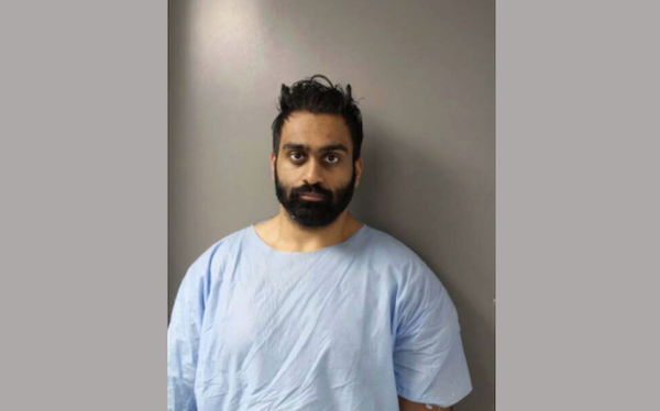 Individual in a loose-fitting blue medical garment poses for an official photograph in front of a gray wall.