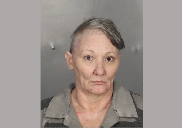 A middle-aged woman in a striped jail uniform, facing the camera for an official booking photograph.