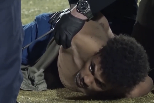 Close-up of a person pinned on the ground on a grassy area as law enforcement officers restrain them.