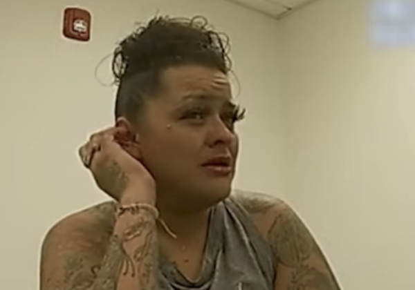 Close-up image of a person with visible arm tattoos sitting at a table in an interview-style setting.