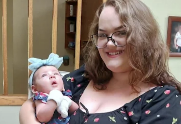 Indoor photo of a woman cradling a baby in her arms near wooden railings.