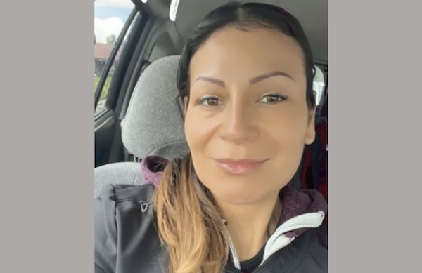 Woman with dark hair pulled back smiles at the camera from a car seat.
