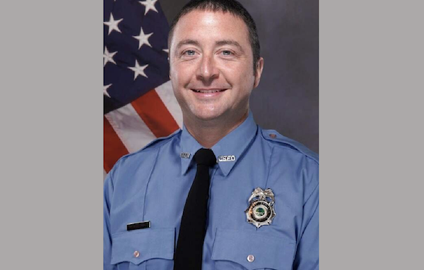 Man in a blue dress uniform and black tie posing for an official photo.