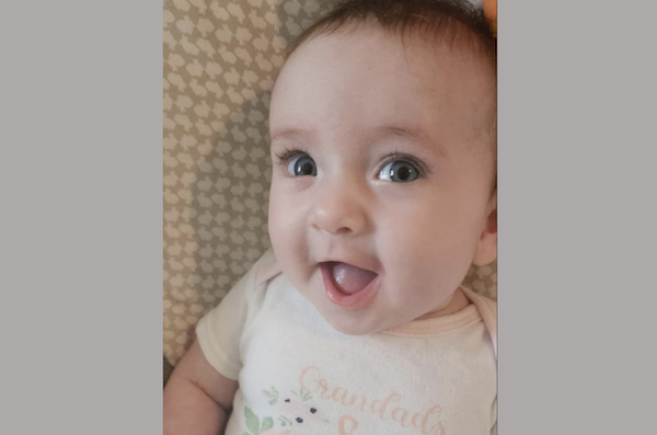 Baby with wide eyes and an open-mouth smile wearing a light-colored onesie.