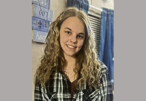 Young woman with wavy light-brown hair smiles toward the camera in a home setting.
