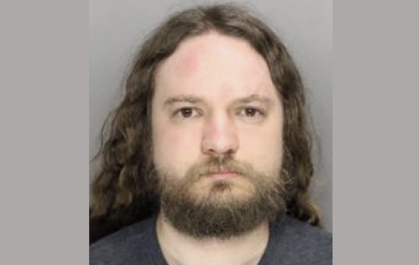 Mugshot-style portrait showing a bearded man with shoulder-length hair and a neutral expression.
