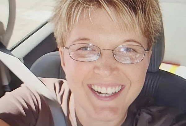Close-up portrait of a smiling person with short hair and wire-frame glasses inside a vehicle.